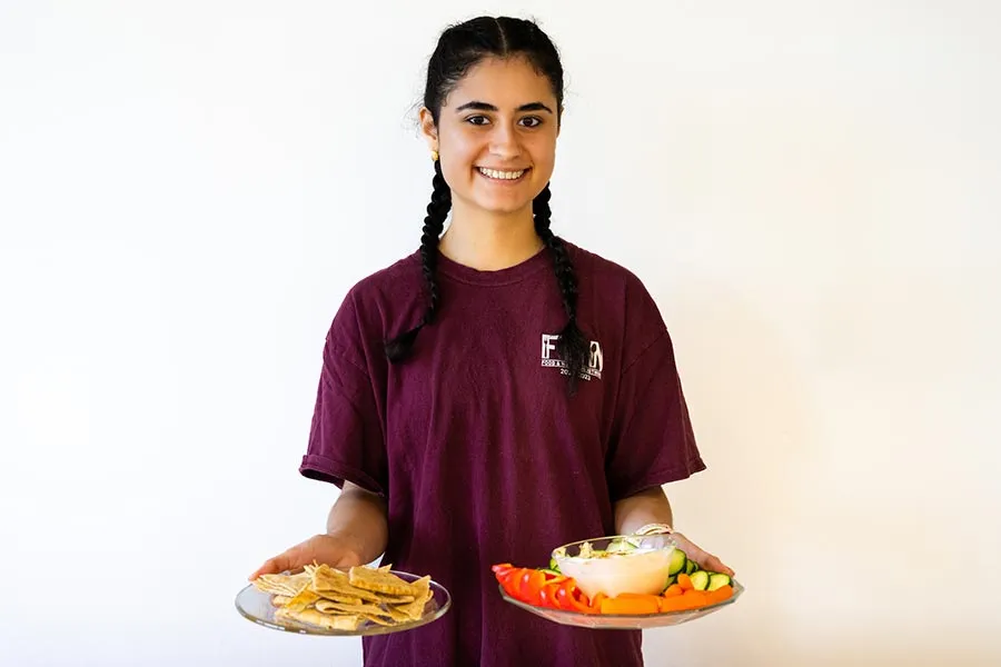 TWU student Mariana Salazar holds two plates with food in front of a white backdrop