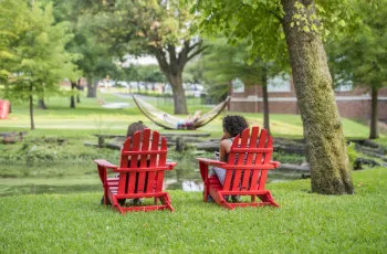 Students sitting in Adirondack chairs looking across a pond to students in hammocks.